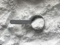 Miarka z białym proszkiem, prawdopodobnie disodium edta, na tle sypkiego materiału.