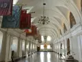 Długi korytarz z łukami i żyrandolami, ozdobiony historycznymi sztandarami. To wnętrze klasztoru na Jasnej Górze, gdzie każdy baner opowiada historię zakonu paulinów.