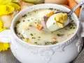 Biały barszcz z jajkiem i kiełbasą, w tle żonkile i cebula. Czym się różni żurek od barszczu białego? Ten pierwszy ma kwaśniejszy smak.