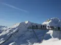 Ludzie na platformie widokowej podziwiają ośnieżone szczyty Alp, jakby byli w świecie Grindelwalda.