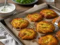 Goldbraune zucchini karotten puffer auf einem Backblech, frisch aus dem Ofen. Dazu ein Dip und frische Kräuter.