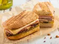 Dos sándwiches cubanos a la parrilla con capas de carne, queso derretido y pepinillos.