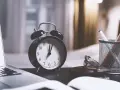 Budzik na biurku obok laptopa i notesu. Zastanawiasz się, po jakim czasie chwilówki oddają sprawę do sądu? Czas ucieka.