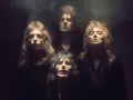 Czterech członków zespołu Queen w mrocznym klimacie, jakby przygotowujących się do wykonania "Bohemian Rhapsody". Ich spojrzenia sugerują głęboką interpretację.