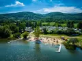Słoneczny dzień nad jeziorem Bielawa. Tłumy plażowiczów, kemping z kamperami i zielone wzgórza w tle.