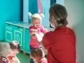 Wesoła dziewczynka z kitkami, pełna energii, pokazuje coś opiekunce. Widać jej radosny temperament dziecka.