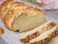 Ein goldbrauner Hefezopf, bestreut mit Zuckerkristallen, liegt auf Backpapier. Ein Stück ist angeschnitten, die weiche Krume ist sichtbar. Ein tolles Rezept für Hefezopf!