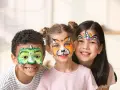 Tre glada barn med ansiktsmålning för halloween: en grön drake, en räv och en enhörning.
