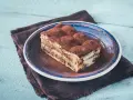 Pyszny kawałek prawdziwego tiramisu, posypany kakao, na niebieskim talerzu.