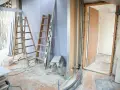 Remont mieszkania w bloku w toku: drabiny, materiały budowlane, widok na drzwi. Czas remontu zależy od zakresu prac.