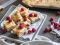 Słodkie brownie i blondie z malinami, pokrojone na kwadraty, ułożone na tacy. Kilka malin rozsypanych obok.