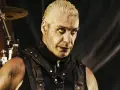 Till Lindemann młody, w skórzanym gorsecie, z mokrymi włosami i intensywnym spojrzeniem, gotowy do występu na scenie.