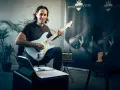 Mann mit E-Gitarre, bereit, online Gitarre zu lernen. Noten und Tablet liegen bereit.