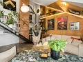 Wygodny salon w stylu loftowym z ceglaną ścianą, metalowymi schodami, wiszącym fotelem i dużą ilością zieleni.