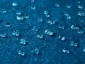 Gouttes d'eau perlant sur un tissu bleu, illustrant comment imperméabiliser un tissu naturellement.