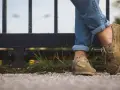Gambe con jeans arrotolati e scarpe senza calzini, appoggiate su un muretto con erba.