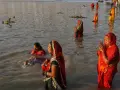 Mujeres rezan en el río Ganges, con vestimentas coloridas y el agua hasta la cintura.