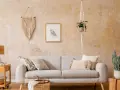 Gemütliches Wohnzimmer mit beiger Wischtechnik Wand, Sofa, Makramee-Deko und Pflanzen.