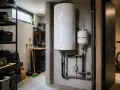 Un boiler bianco e un serbatoio di espansione, collegati da tubi, illustrano la differenza tra caldaia e scaldabagno in un locale tecnico.