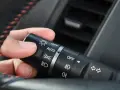 Dłoń ustawia przełącznik świateł w samochodzie, wybierając, na jakich światłach się jeździ: AUTO, OFF, światła mijania lub drogowe.