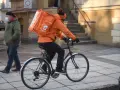 Kurier rowerowy w pomarańczowej kurtce z plecakiem Pyszne.pl, zarobki zależą od liczby dostaw.