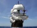 Un majestueux galion espagnol navigue sous un ciel bleu, ses voiles blanches gonflées par le vent.