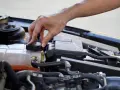A hand twists the cap on a car's coolant reservoir, a step in learning how to dispose of antifreeze safely.