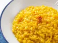 Un cremoso risotto alla milanese, giallo intenso grazie allo zafferano, guarnito con fili rossi.
