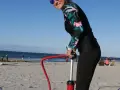 Frau pumpt SUP auf. Am Strand bereitet sie sich auf Wassersport vor.