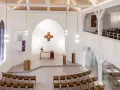 Moderner Aufbau evangelische Kirche mit Holzkreuz, Altar, Kanzel und vielen Sitzplätzen.