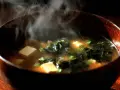 Gorący, parujący sos z pasty miso w drewnianej misce, z kostkami tofu i wodorostami.