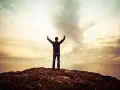 Mann mit erhobenen Armen auf einem Felsen, blickt auf das Meer. Ein Gefühl des aaronitischen Segens liegt in der Luft.
