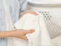 Ręce trzymają białą tkaninę z plamami po podkładzie. Dowiedz się, jak usunąć plamy z podkładu i przywrócić ubraniom nieskazitelny wygląd.