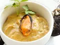 Paté de mejillones cremoso en cuenco blanco, decorado con perejil y mejillones enteros al lado.