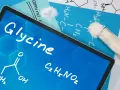 Tablet z napisem "Glycine", wzorem chemicznym i próbówką z proszkiem. Informacje o glicynie i jej dawkowanie.