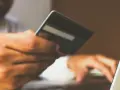 Mężczyzna z kartą płatniczą przy laptopie, zapewniający sobie bezpieczne zakupy w internecie.