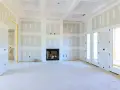 Interno di una casa in costruzione con pareti e soffitto in cartongesso, camino e porte a doppio battente.