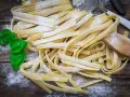 Świeży, domowy makaron bez glutenu, posypany mąką, z listkami bazylii i drewnianą łyżką.