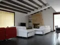 Soffitto con travi in legno scuro, un camino in pietra e divani bianchi. Ecco come fissare travi in legno al soffitto per un effetto rustico.