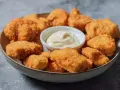 En skål med gyllene, krispiga chicken nuggets och en liten skål med krämig dippsås. Perfekt för en snabb och god måltid.