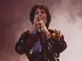 Freddie Mercury śpiewa z pasją, czując, że chce się uwolnić. Błyszcząca kurtka odbija światła sceny.