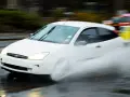 Auto bianco in movimento su strada bagnata, con un'enorme spruzzata d'acqua che indica l'aquaplaning cos'è.