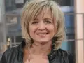 Uśmiechnięta Małgorzata Bogdańska w czarnej ramonesce, z blond włosami i delikatnym makijażem.