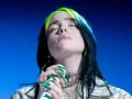 Piosenkarka Billie Eilish z zamkniętymi oczami śpiewa do mikrofonu, jej zielone pasemka włosów lśnią.