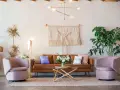 Salon moderne avec canapé en cuir marron, fauteuils roses poudrés, tapis texturé et macramé mural. La couleur peinture salon est neutre, mettant en valeur les meubles.