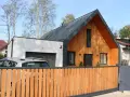 Nowoczesny dom z drewnianą dobudówką do części murowanej. Obok garaż, przed którym stoi samochód.