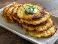 Pile de galettes de pomme de terre dorées et croustillantes, garnies d'une cuillère de crème fraîche et de ciboulette.