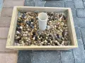 Base per ombrellone fai da te: un contenitore in legno riempito di ghiaia con un tubo centrale per l'asta.