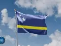 Flaga Curacao powiewa na wietrze na tle błękitnego nieba z białymi chmurami. Dwie białe gwiazdy na niebieskim tle i żółty pas.