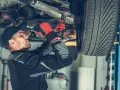 Mechanik w rękawicach dokręca sworzeń zwrotnicy w podwoziu samochodu.